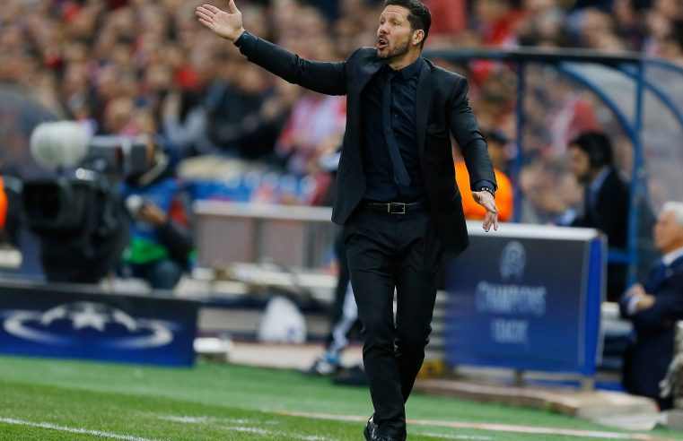 Diego Simeone in the black suit walking down the pitch line during the match